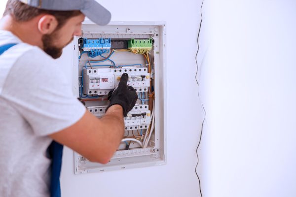 Electrical technician in uniform looking focused while working in a switchboard with fuses. Manual work, maintenance, repair service concept