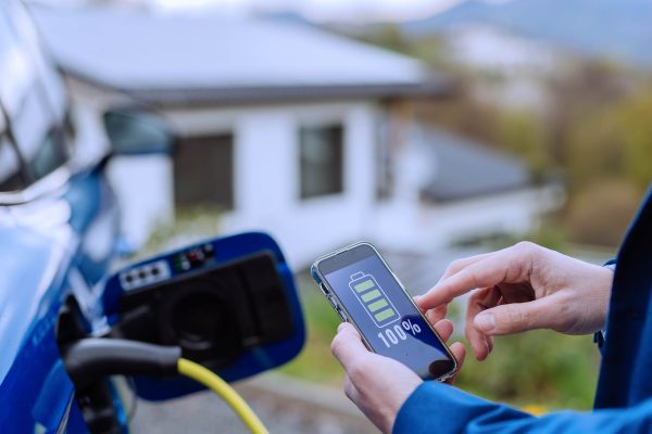 Close up of businessman holding phone, checking charging of his electric car.